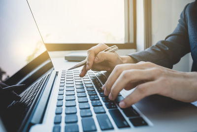 Cropped hands of businesswoman using laptop while sitting at office