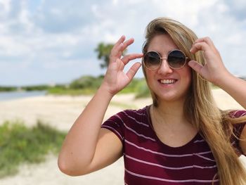 Portrait of young woman wearing sunglasses standing against sea