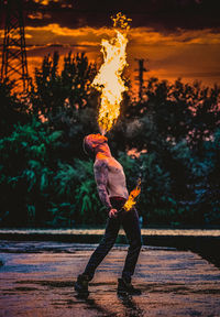 Side view of shirtless man breathing fire against trees