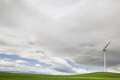 Wind turbines on field against cloudy sky