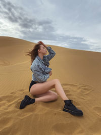 Yong woman sitting on sand at desert