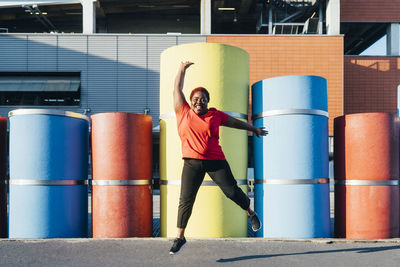 Happy woman with hand raised jumping on footpath