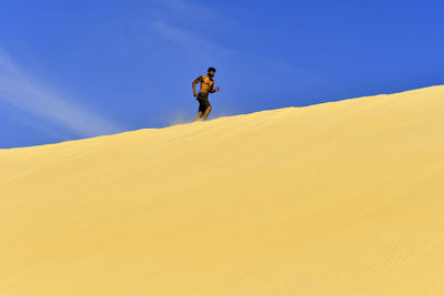 Man on sand dune in desert against clear blue sky