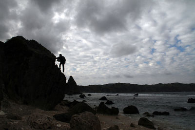 Man standing on rock by sea against sky