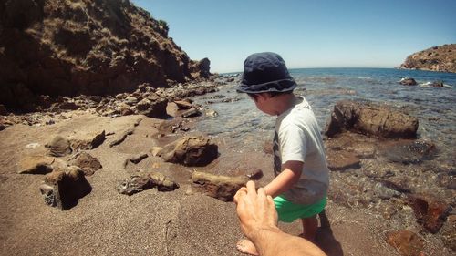 Cropped image of person holding boy hand at shore