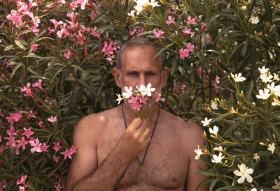 Portrait of shirtless man standing by flowering plants