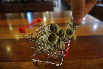 Cropped hand picking paper currency from toy shopping cart at table