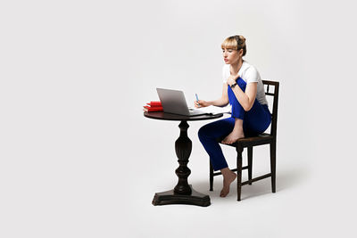 Portrait of young woman using laptop while sitting against white background