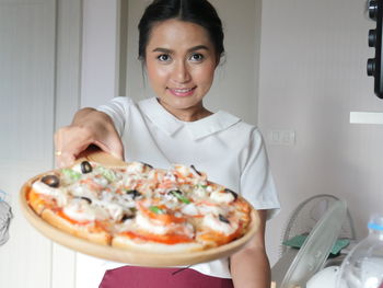 Portrait of young woman holding pizza at home