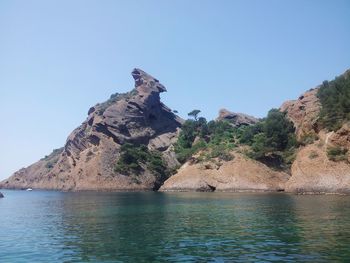 Rock formation by sea against clear sky