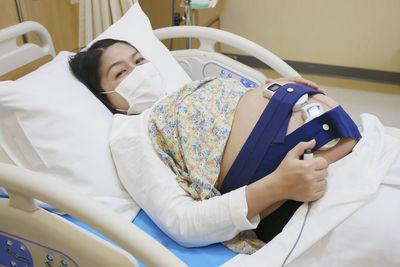 Asian pregnant woman wear face mask hold pressing emergency call remote button 