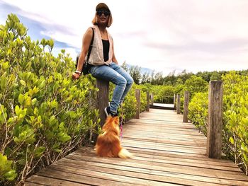 Woman with dog on boardwalk against sky