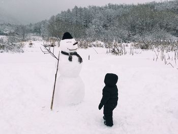 Side view of boy standing by snowman on field