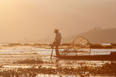 Man fishing in inle lake against sky during sunset