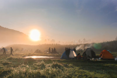 Hikers with tent on field against sky