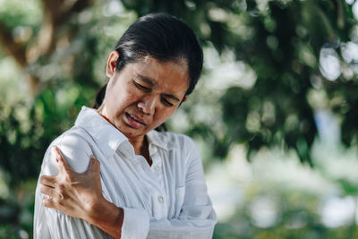 Woman with arm pain standing against trees