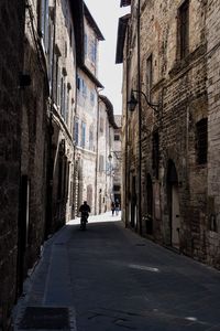 Rear view of man walking on narrow street amidst buildings