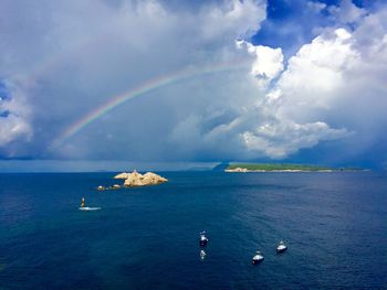 Scenic view of rainbow over sea peppered with boats against cloudy sky