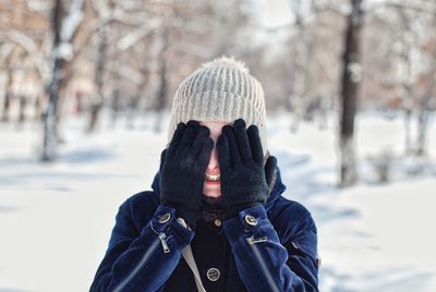 Happy woman covering eyes with hands in forest during winter