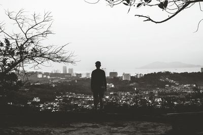 Rear view of man standing by cityscape against sky