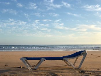 Deck chairs on beach against sky