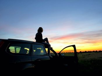 Silhouette woman on car against sky during sunset