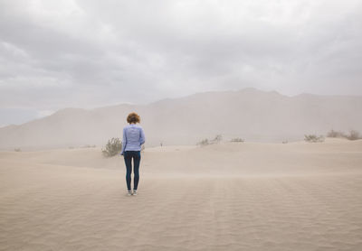 Rear view of woman standing on sand dune