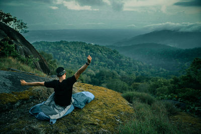 Man stretching hands on mountain against sky