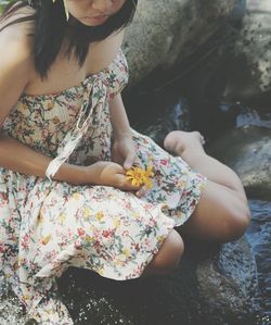 High angle view of young woman holding flowers while sitting on rock