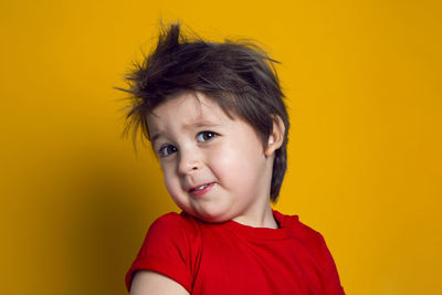 Cheerful baby boy in red t-shirt stands on yellow background