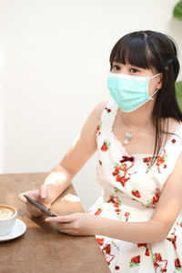 Woman wearing mask using mobile phone at table