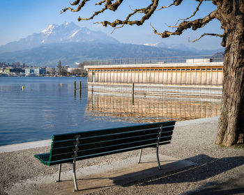 Empty bench by lake against sky