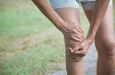 Close-up of person holding knee while standing on land