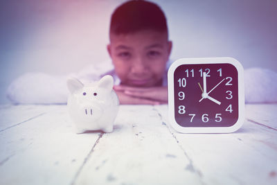 Portrait of teenage boy by piggy bank and clock on table