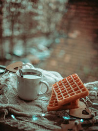 Close-up of coffee cup with waffle on table