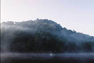 Scenic view of lake and mountains against sky during foggy weather