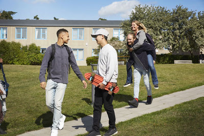 Man piggybacking woman while walking with friends at university campus on sunny day