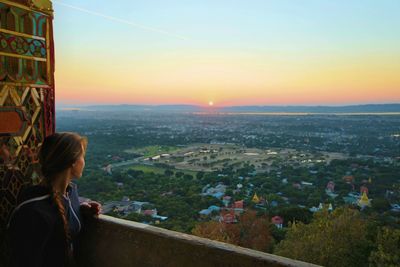 Woman standing by cityscape against sky during sunset