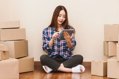 Young woman using digital tablet sitting on floor at new home