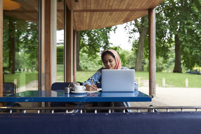 Young woman wearing hijab studying with her laptop on a terrace of a cafe