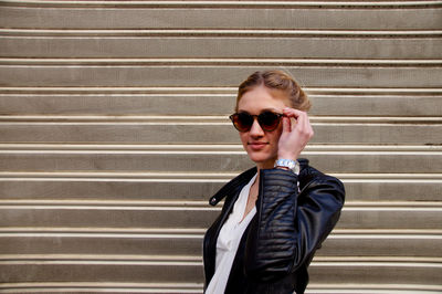 Young woman wearing sunglasses while standing against closed shutter