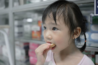 Close-up of girl eating food while standing by shelves