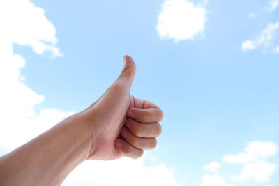 Cropped hand gesturing thumbs up sign against sky