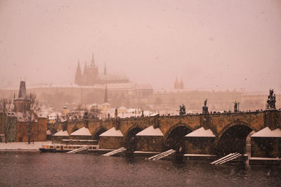 City by river during winter against sky