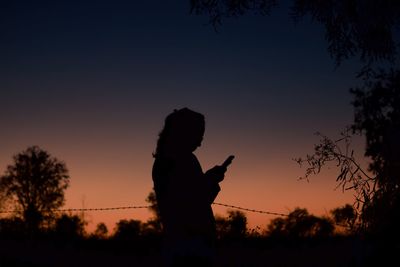 Silhouette woman standing by plants against sky during sunset