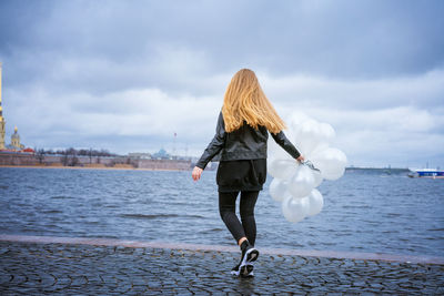 Caucasian girl holding white balloons standing by the river on the embankment