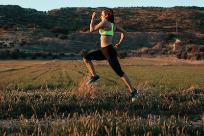 Side view of woman running on field during sunset
