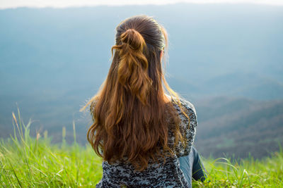 Woman sitting on grassy field against mountains