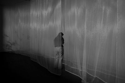 Rear view of woman standing by curtain