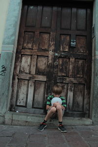 Full length of boy holding ball while sitting against closed doors